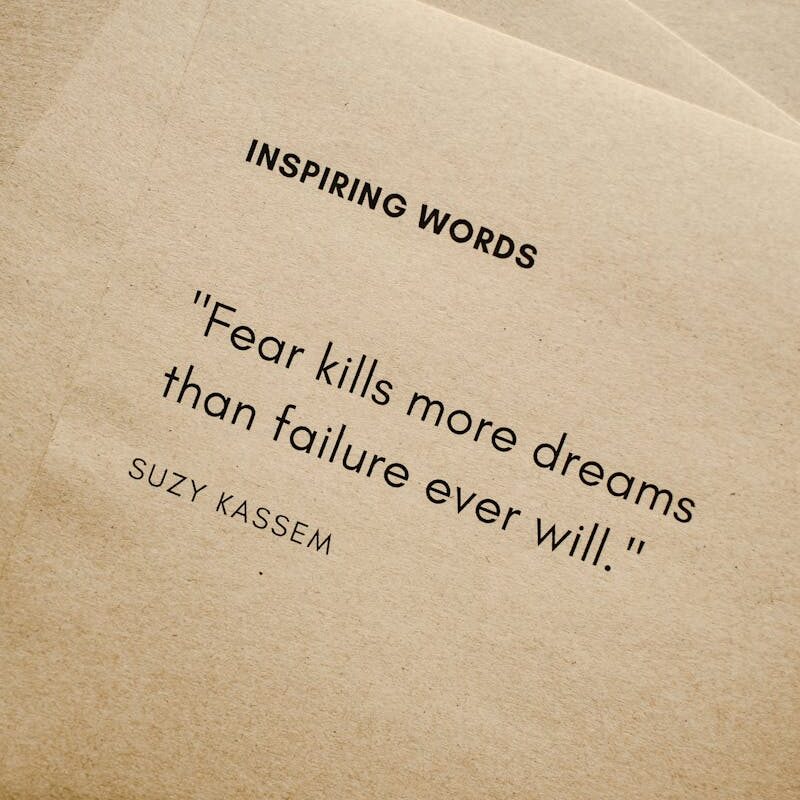 Motivational quote 'Fear kills more dreams than failure ever will.' by Suzy Kassem on paper texture.